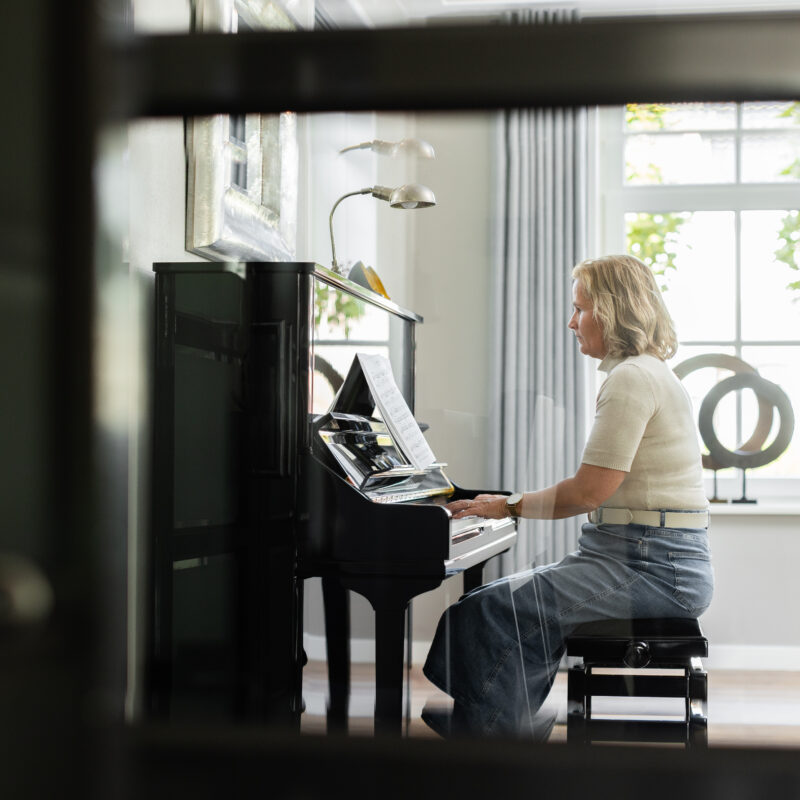 Annelies aan de piano in een lichte ruimte, symbool voor rust, reflectie en persoonlijke ontwikkeling in coaching.