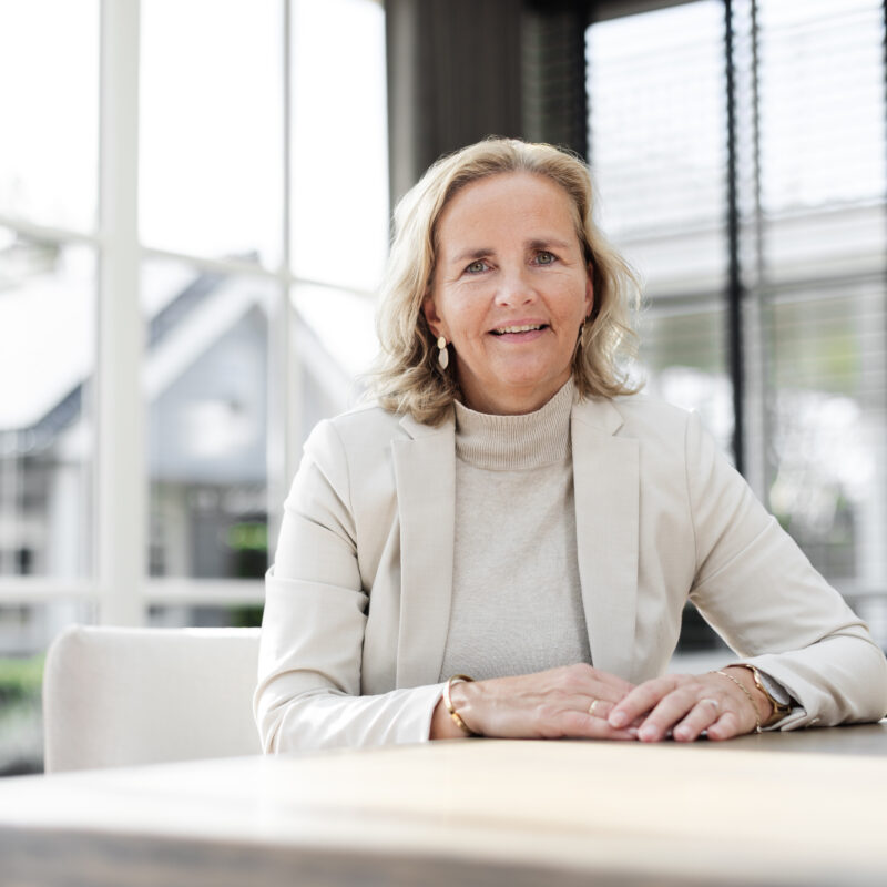 Annelies in een lichte ruimte, rustig en vriendelijk aan tafel.